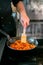 Crop chef cooking vegetables in frying pan