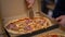 Crop chef slicing ham pizza in pizzeria