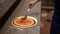 Crop chef spreading tomato sauce on pizza in restaurant kitchen