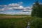 A crop field with clouds and a small river with a footbridge