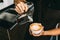 Crop image of a young male barista pouring hot milk into hot espresso black coffee for making Latte Art