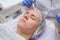 Crop master applying white mask with brush on face and neck of young woman in towel lying on table