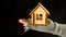 Crop person with wooden toy house on black background. Top view of crop anonymous person holding small wooden toy house