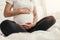 Crop pregnant woman sitting on bed