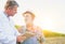 Crop scientist showing digital tablet to senior farmer against corn field with yellow lens flare