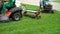 Crop shot of workers riding on industrial lawn mowers and cutting grass in park