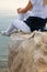 Crop view of attractive young woman sitting at seaside cliff edge