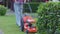 Crop view of female gardener in jeans mowing lawn with equipment on backyard.