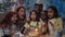 Crop view of little child opening eyes and blowing candles on cake while having party. Diverse ethnicity man, woman and