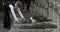 Crop view of teen boy in suit putting white lily flowers on gravestone of his dad . Teenager kid honoring his father