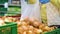 Crop woman in medical gloves putting onions in plastic bag at grocery store