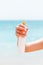 Croped image of woman`s hand holding sunscreen spray at the sea background