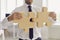 Cropped businessman or company manager in office wear joining two pieces of jigsaw puzzle
