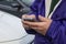 Cropped close-up of man in purple jacket holding a phone in front of parked cars - selective focus