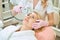 Cropped female cosmetologist doing laser depilation of forehead of adult woman