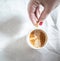 Cropped female hands with red manicure hold a chuck with cappuccino coffee on a light white retro sloppy background