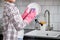 Cropped female rinsing dishes with purple sponge above kitchen sink