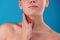 Cropped frontview of model touching her face and neck tenderly. Feminine hands with accurete nails on blue studio