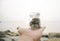 Cropped hand holding transparent glass jar with coin.blur background at the beach