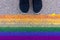 Cropped humans legs in black shoes standing on asphalt in front of lgbt rainbow colored flag, gender identity and self-