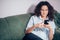 Cropped image of adult with curly hair sitting on the grey sofa with phone