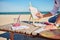 Cropped image of artist`s hand holding paintbrush and painting boat with watercolors, sitting on a wooden chaise lounge with sea