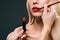 cropped image of beautiful blonde hair girl with visagiste applying lipstick with brush,