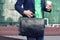 Cropped image businessman in casual wear tries to hold up cup of coffee to go, leather briefcase and smartphone at the same time