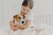 Cropped image of caring little girl in white t shirt, cuddles small pedigree dog, expresses big love to animal, poses on bed in