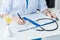 cropped image of female doctor writing in clipboard at table with stethoscope