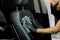 Cropped image of hand of auto service worker, in black rubber glove, cleaning car interior, car front seat with