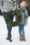 Cropped image of legs of mother and son, holding together beautiful Christmas wreath, standing outdoors in winter park