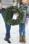 Cropped image of legs of mother and son, holding together beautiful Christmas wreath, standing outdoors in winter park