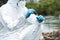 cropped image of male scientist in protective suit and mask putting sample of soil by tweezers in test flask