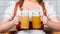 cropped image of oktoberfest waitress in traditional bavarian dress holding mugs of light beer with foam