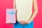 Cropped image of pink spotted gift box in pregnant woman`s hand against her belly at pink background. Future mother in colorful