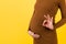 Cropped image of positive pregnant woman in brown dress showing okay gesture against her belly at yellow background. Easy and