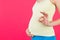 Cropped image of positive pregnant woman in colorful home clothing showing okay gesture against her belly at pink background. Easy