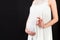 Cropped image of positive pregnant woman in white dress showing okay gesture against her belly at black background. Easy and happy