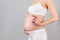 Cropped image of positive pregnant woman in white underwear showing okay gesture against her belly at gray background. Easy and