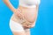 Cropped image of pregnancy belt dressed on suffering pregnant woman in underwear for reducing pain in the back at blue background