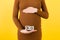 Cropped image of pregnant woman in brown dress showing thirty weeks of pregnancy cubes at yellow background. Waiting for a baby.