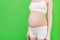 Cropped image of pregnant woman`s belly at green background. Future mom in white underwear. Parenthood concept. Copy space