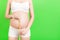 Cropped image of pregnant woman in white underwear measuring her growing abdomen at green background. Inch tape measure. Copy