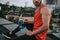 cropped image of sportsman sitting on roof railing with bottle