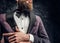 Cropped image of a stylish bearded man dressed in a violet elegant suit standing against a dark textured wall