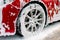 Cropped image of wheel of luxury red car in outdoors self-service car wash, covered with cleaning soap foam