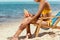 cropped image of woman applying sunscreen lotion on skin while sitting on deck chair on sandy