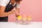Cropped image of woman bakery decorating muffins with rosy cream using pastry cone, delicious dessert on glass plate, faceless