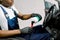 Cropped image of young African male car detailing worker, sitting inside of modern vehicle, and cleaning car dashboard